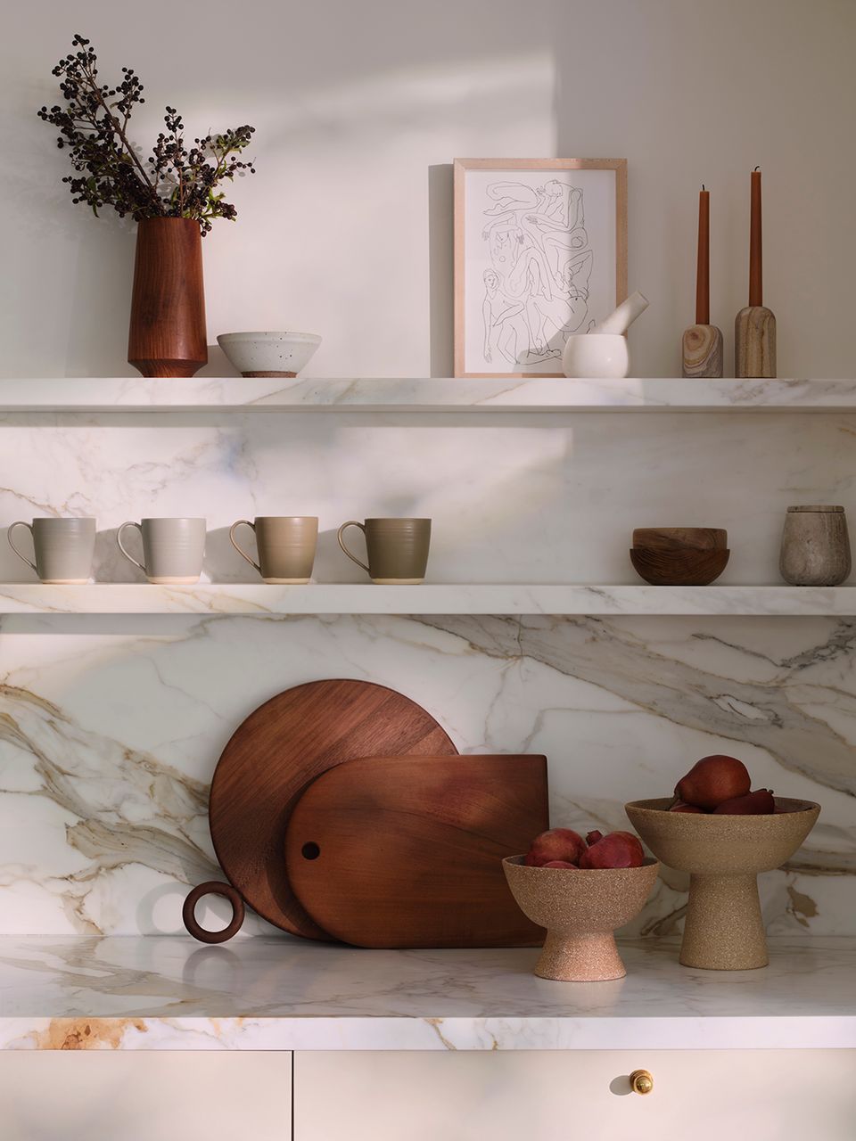 Minimalist kitchen with marble countertop, white shelving, warm ceramic vessels, and earthy natural tones
