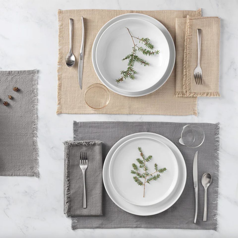 Sustainable table setting with white plates, linen placemats in beige and gray, botanical garnish details