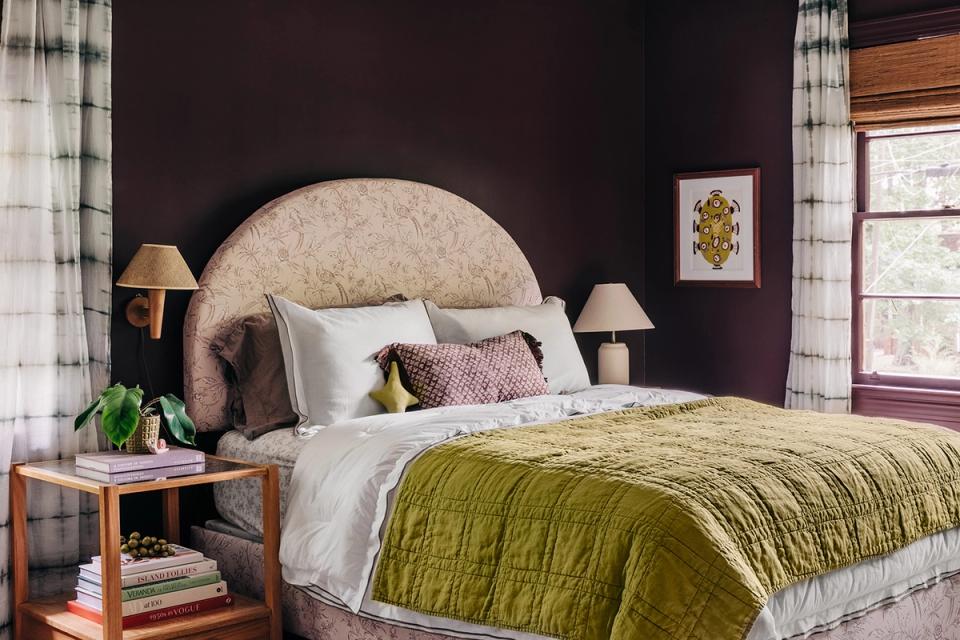 Eclectic maximalist bedroom with deep plum walls, mustard throw, and round upholstered headboard