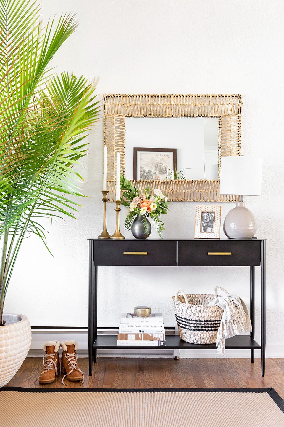 Modern boho hallway featuring black console with natural woven mirror, potted palm, and curated accessories in warm earth tones