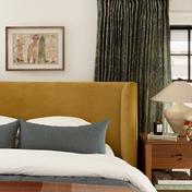 Mid-century bedroom with mustard upholstered headboard, sage green curtains, and warm wood nightstand