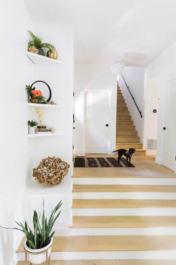 Scandinavian entryway with white walls, light oak stairs, stacked floating shelves with greenery, and airy Nordic aesthetic throughout.