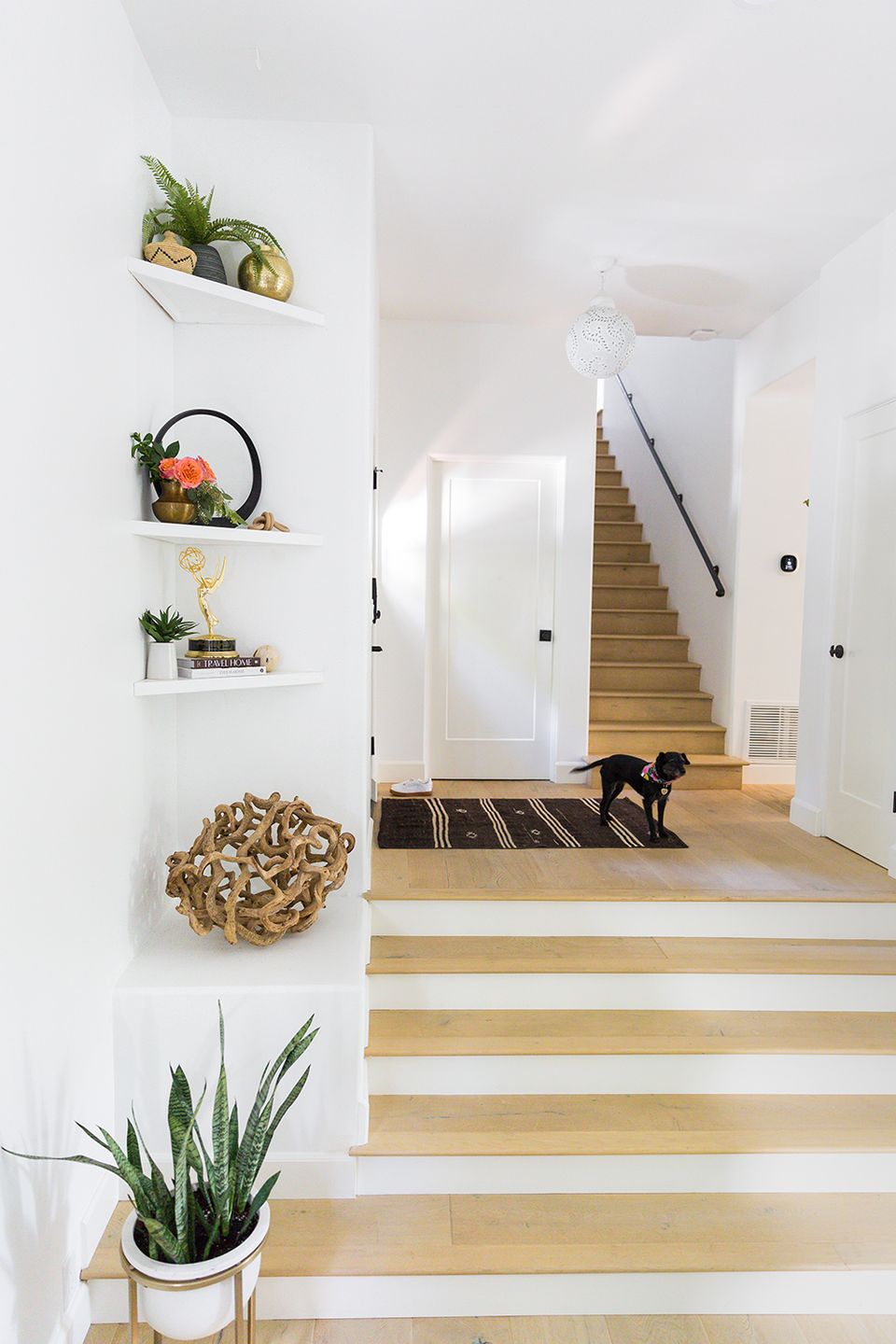 Scandinavian entryway with white walls, light oak stairs, stacked floating shelves with greenery, and airy Nordic aesthetic throughout.
