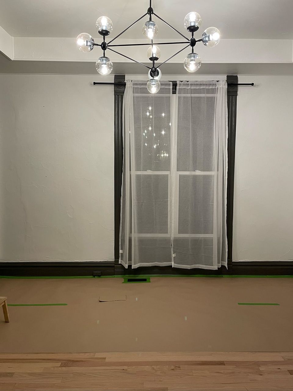 Modern statement dining space with contemporary glass chandelier, neutral walls, and sheer curtains emphasizing architectural drama and elegance