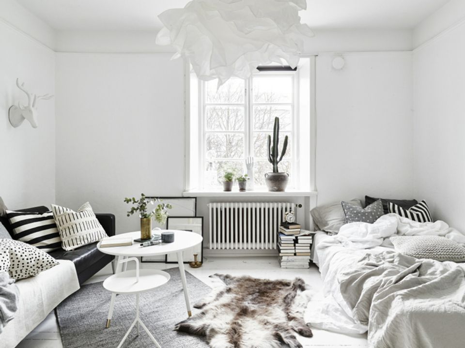 Serene Scandinavian bedroom with white walls, natural light, potted plants, and soft neutral bedding creating calm simplicity.