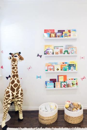 Playful nursery reading nook with giraffe figure, floating shelves of colorful children's books, and woven baskets
