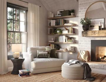 Modern minimalist reading room with cream upholstery, fireplace, white shelving, and natural light from floor windows