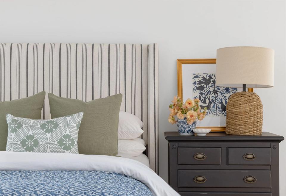 Preppy bedroom featuring vertical striped headboard, sage green accents, patterned throw pillows, and black nightstand for energetic yet refined style.