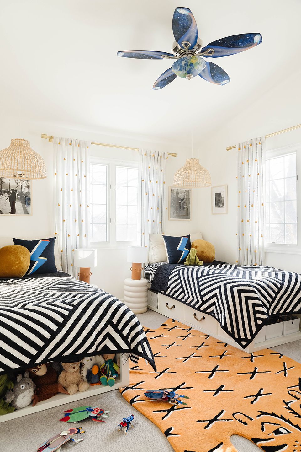 Twin bedroom with bold black-and-white striped bedding, blue ceiling fan, and hidden toy storage under beds.