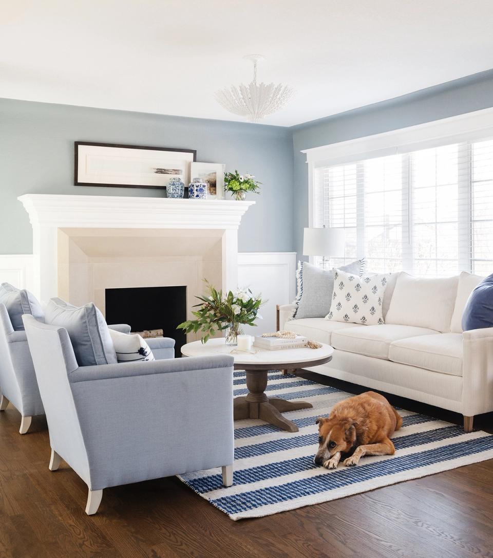 Classic coastal living room with soft blue walls, white fireplace, and light-filled windows