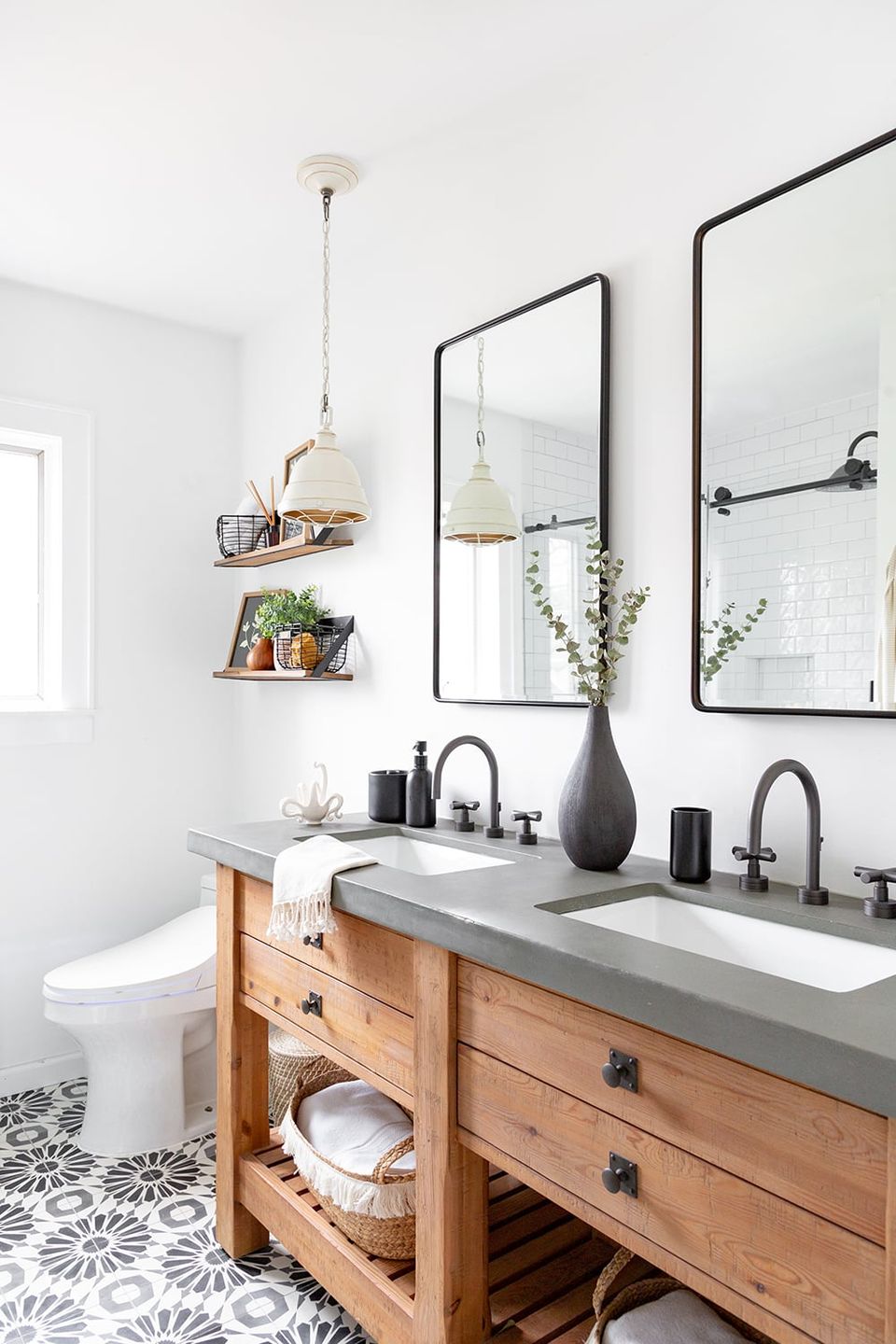 Scandinavian bathroom with warm wood vanity, concrete countertop, black-framed mirrors, and monochromatic patterned floor tiles