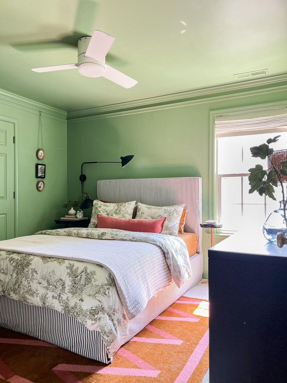 Cheerful mint green bedroom with striped upholstered bed, coral accents, and bright geometric area rug
