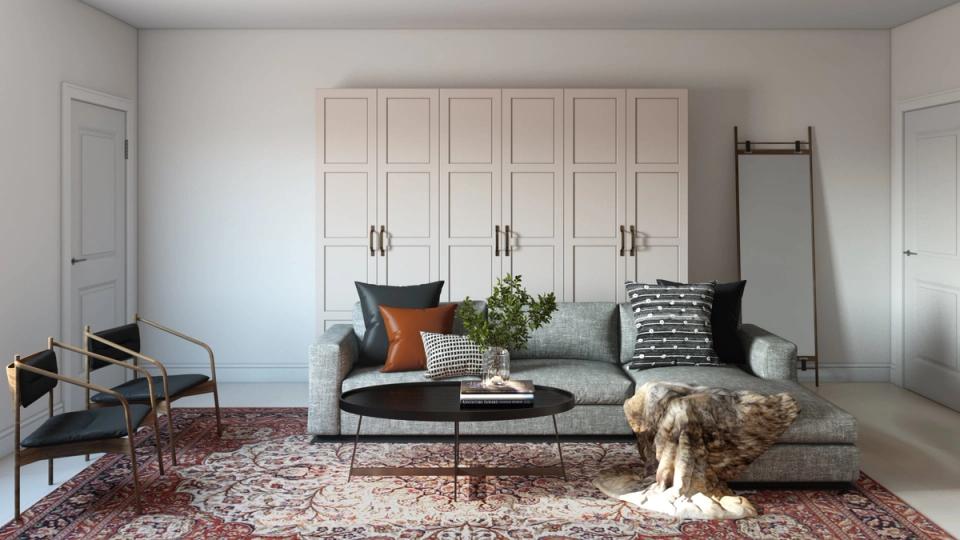 Minimalist living room with cream paneled wall, gray sofa, warm terracotta accents, and vintage-inspired furnishings on burgundy area rug.