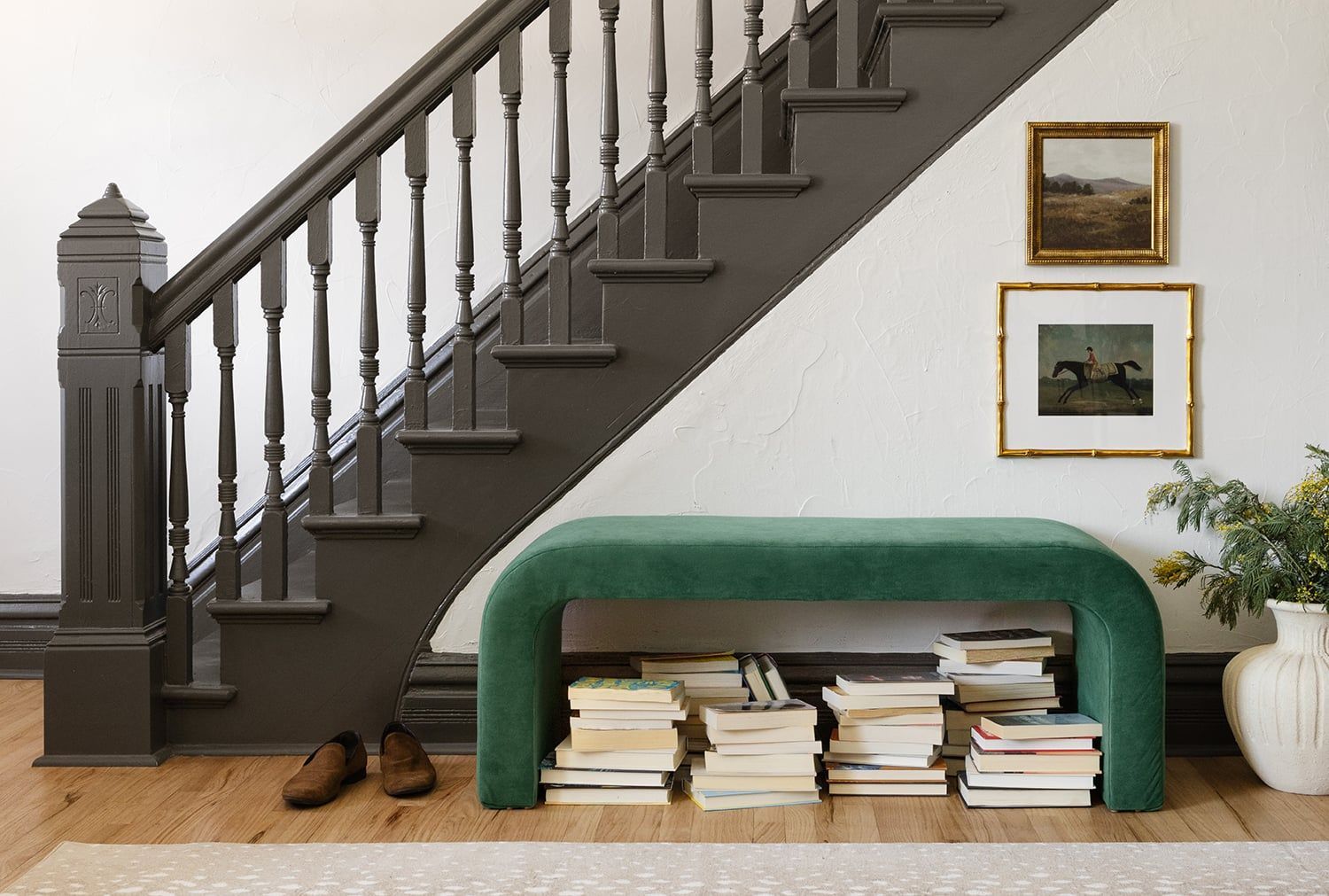 Sophisticated entryway featuring emerald arched bench, dark staircase, and gallery-style framed art