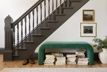 Sophisticated entryway featuring emerald arched bench, dark staircase, and gallery-style framed art