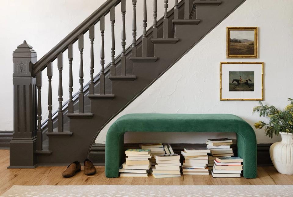 Sophisticated entryway featuring emerald arched bench, dark staircase, and gallery-style framed art