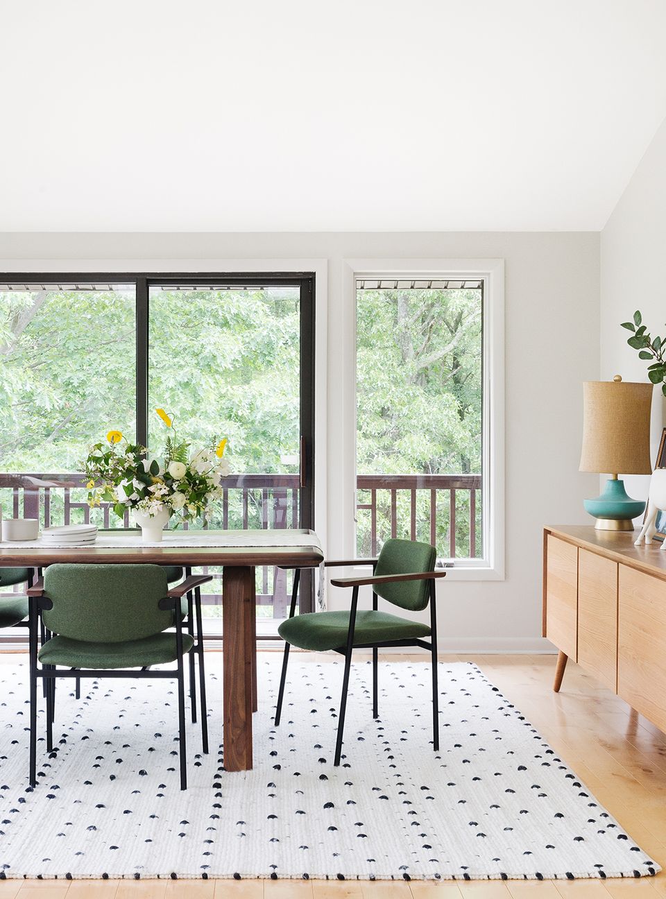 Mid-century modern dining space with green chairs, patterned rug, and forest views