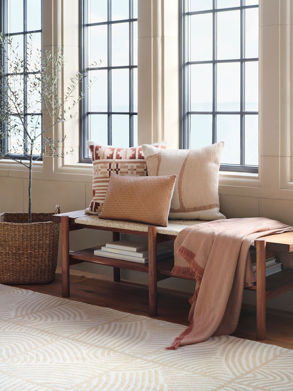 Serene window nook with warm peachy tones, textured pillows, wooden bench, and minimalist coastal style