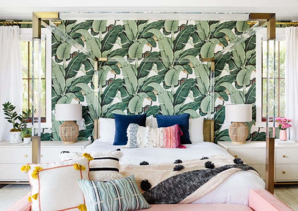 Tropical bohemian bedroom with bold botanical wallpaper, brass four-poster bed, and vibrant jewel-tone accents
