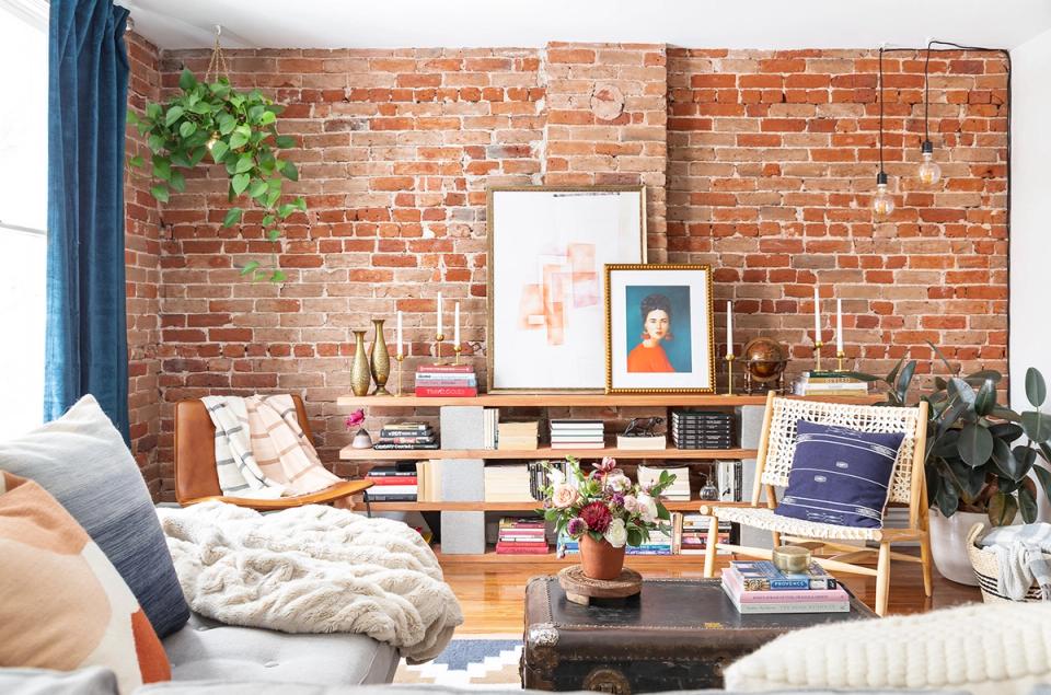 Industrial boho living room with exposed red brick, cream sectional, navy accents, and layered shelving display
