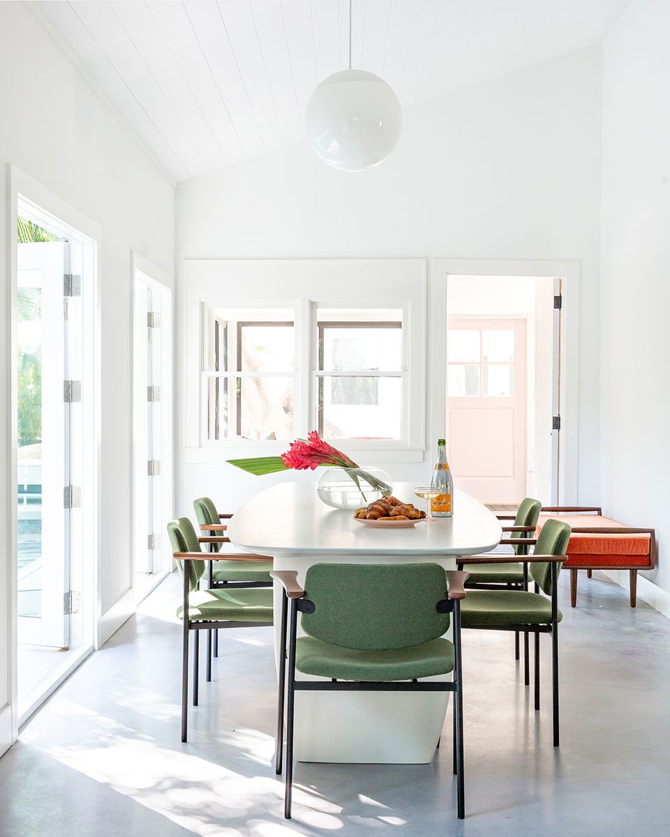 Airy Scandinavian-inspired dining space with forest green chairs, round pendant light, and abundant natural illumination from glass doors