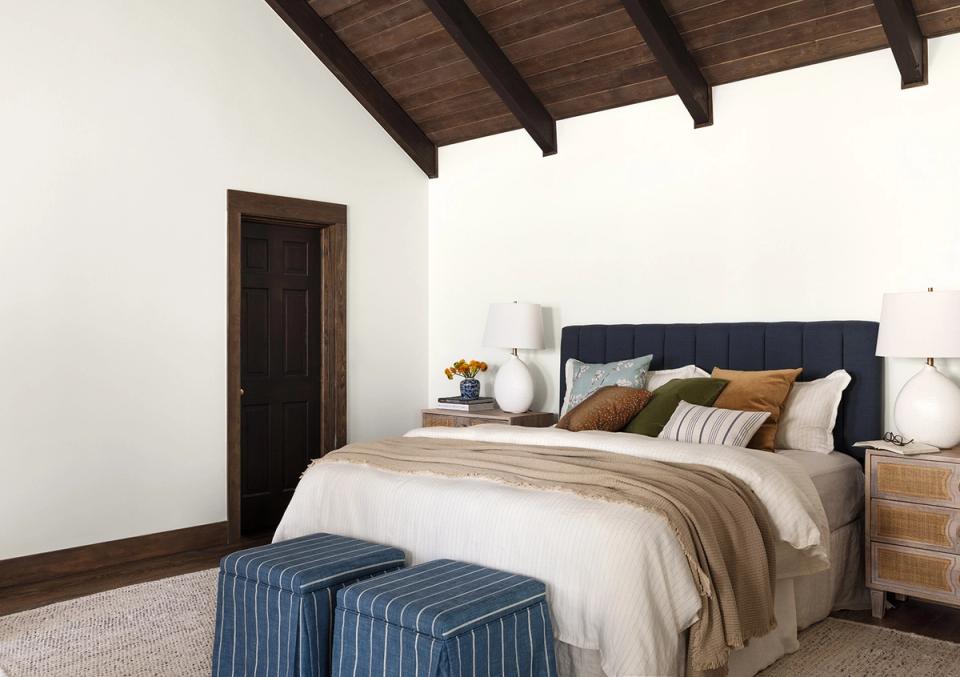 Rustic modern bedroom with dark wood beams, navy headboard, warm earth tones, and relaxed elegance
