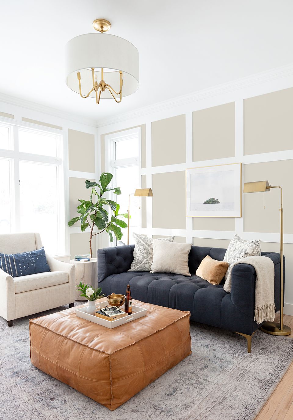 Modern living room with navy sofa, leather ottoman, cream walls, and brass lighting fixtures