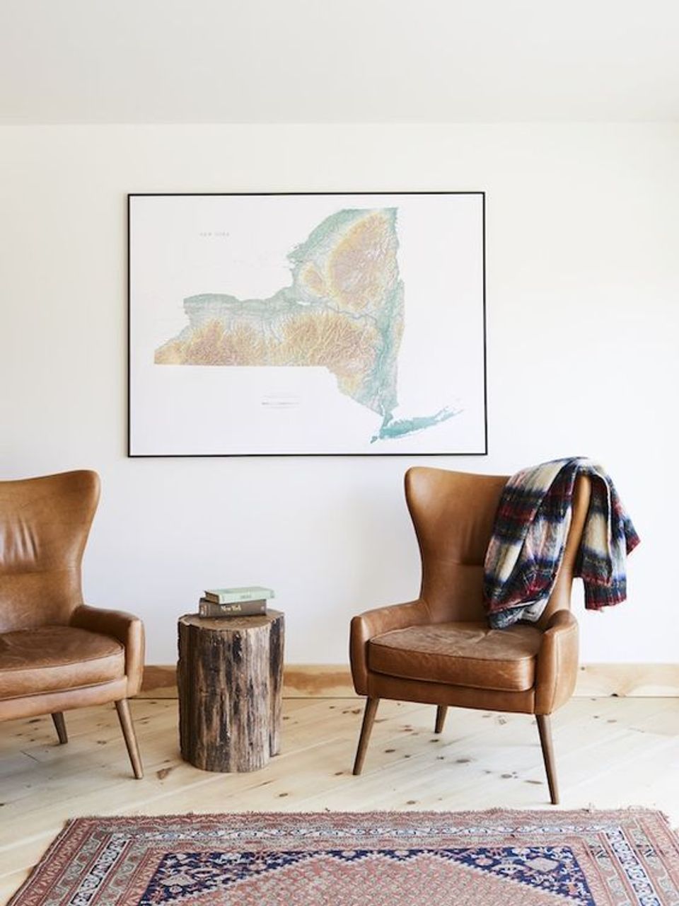 Minimalist cabin seating area with cognac leather chairs, vintage wood stump table, and map art