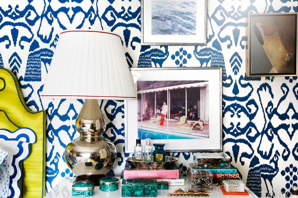 Eclectic maximalist desk with bold blue and white geometric wallpaper, vintage photography, stacked books, and brass lamp