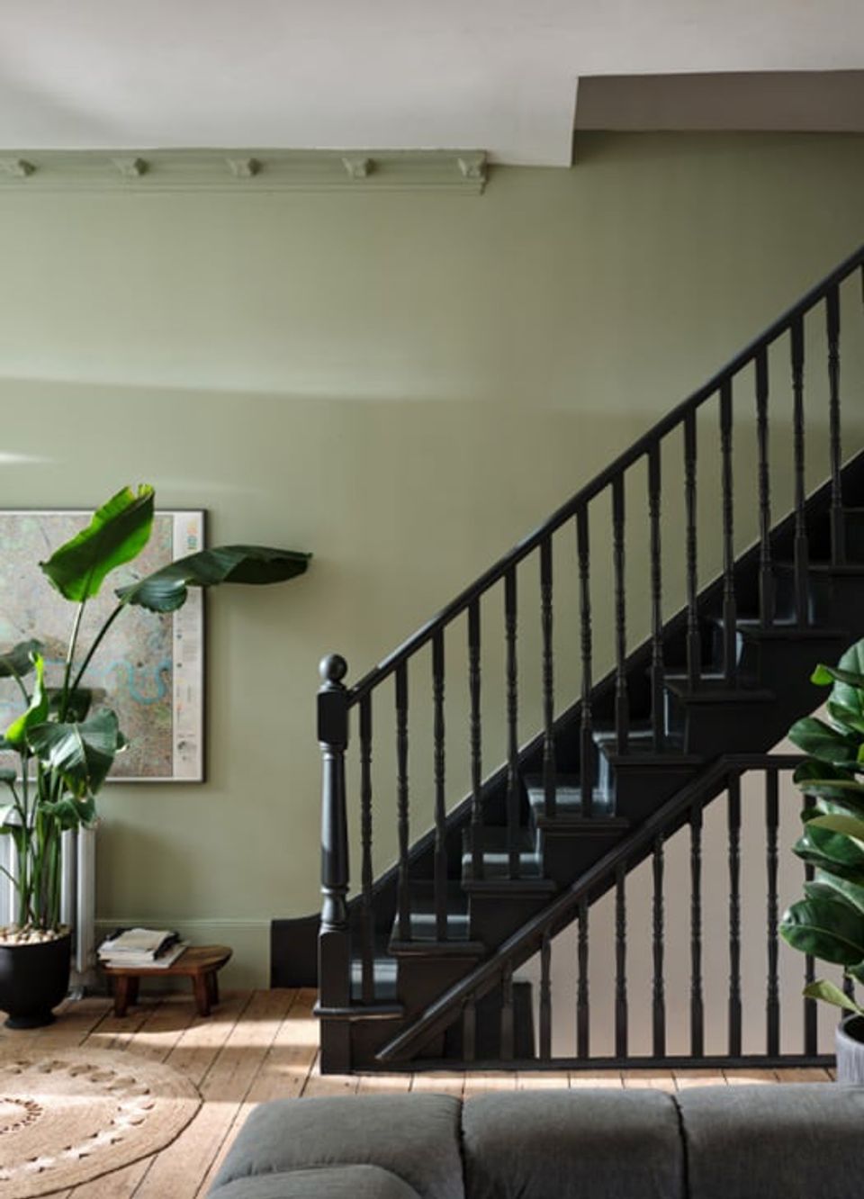 Serene sage green entryway with black staircase, natural light, and potted plants creating a calm, modern botanical aesthetic