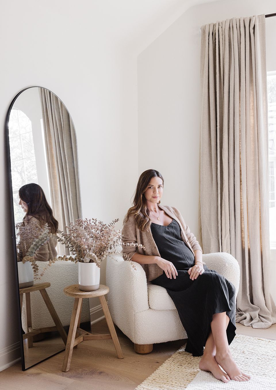 Serene bedroom corner with arched mirror, cream armchair, and floor-to-ceiling linen curtains in warm taupe tones creating a Texas modern aesthetic