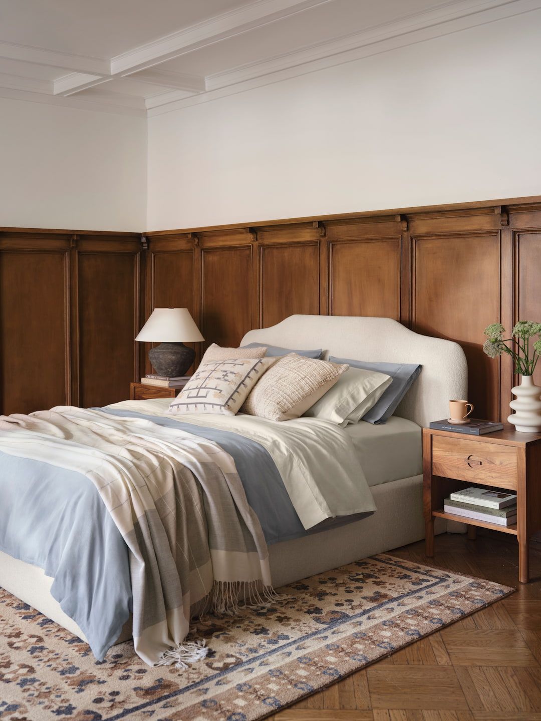 Bedroom with a cream upholstered bed, a wood-paneled wall, and a patterned rug