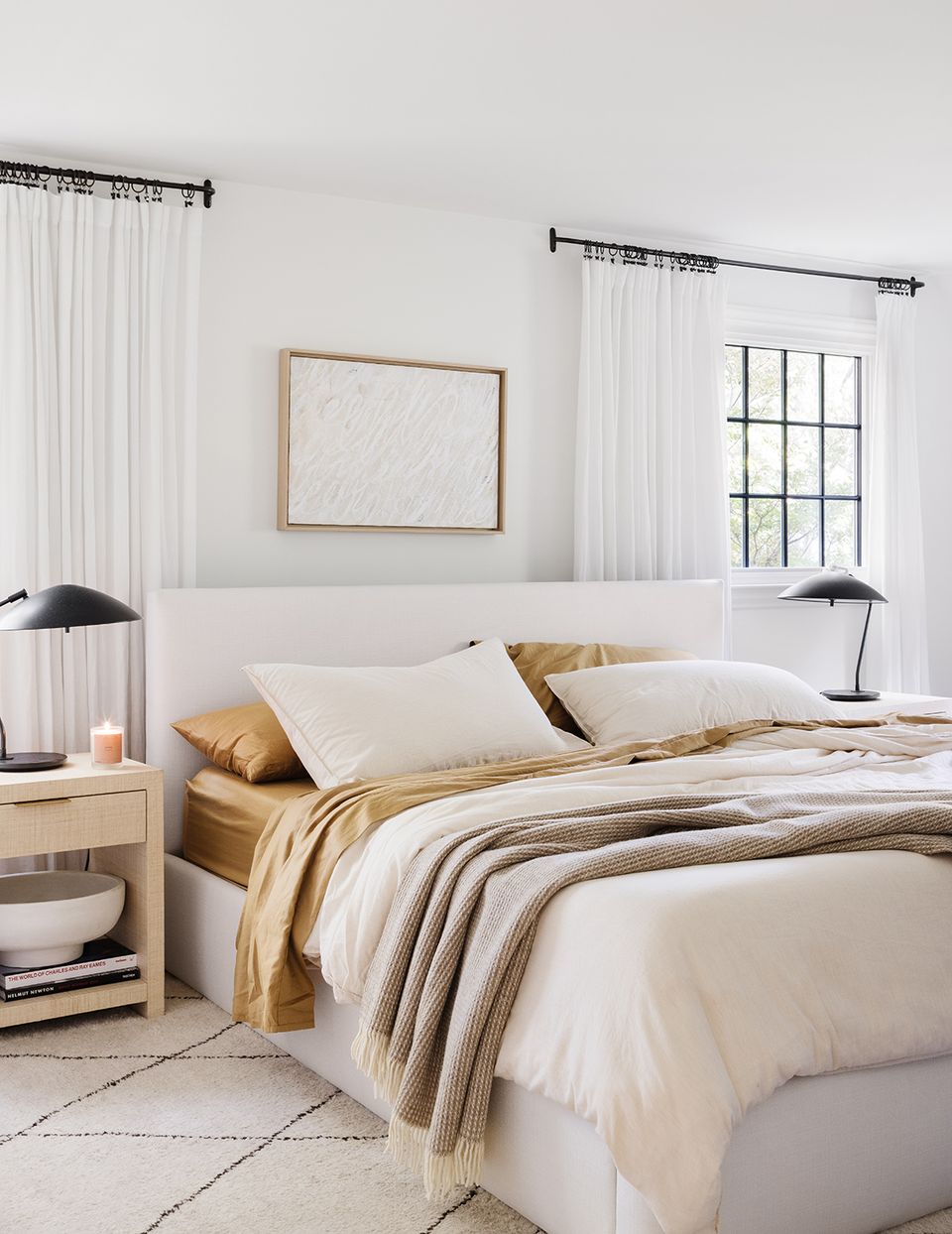 Luxe neutral bedroom with white headboard, gold bedding, and black metal lamps.