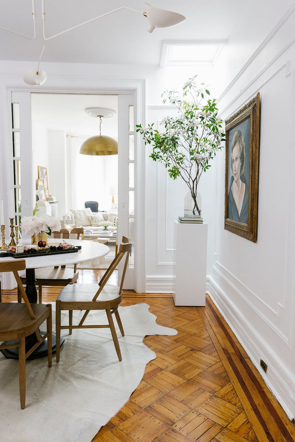 Minimalist dining room with warm wood tones, brass pendant, white walls, and curated greenery emphasizing elegant simplicity.