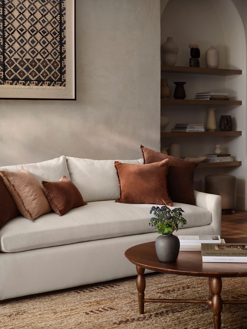 Minimalist lounge with cream curved sofa, rust velvet pillows, and floating wood shelves