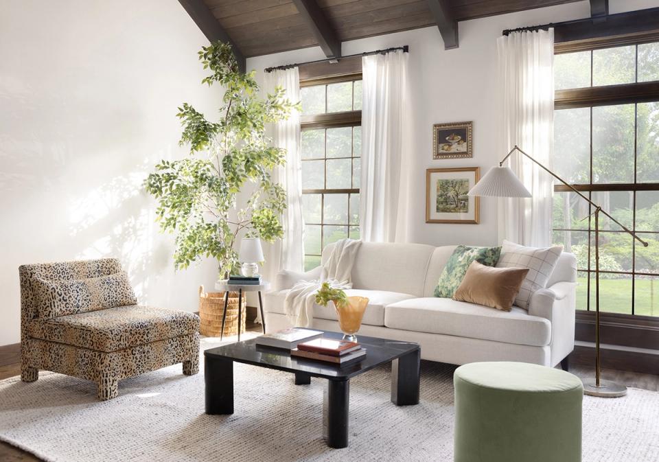 Modern rustic living room with dark wood ceiling beams, textured seating, and lush greenery