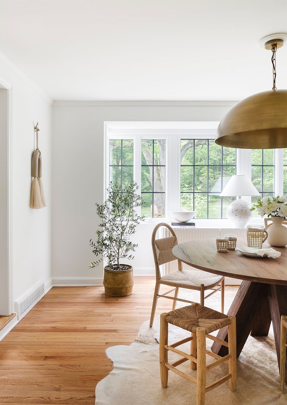 Bright dining nook with brass pendant, natural wood chairs, and abundant natural light