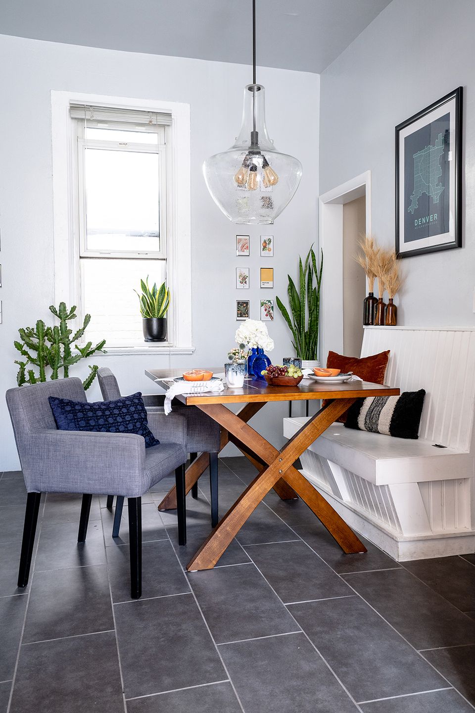Scandinavian nook with wood X-frame table, navy chair, potted plants, and pendant lighting