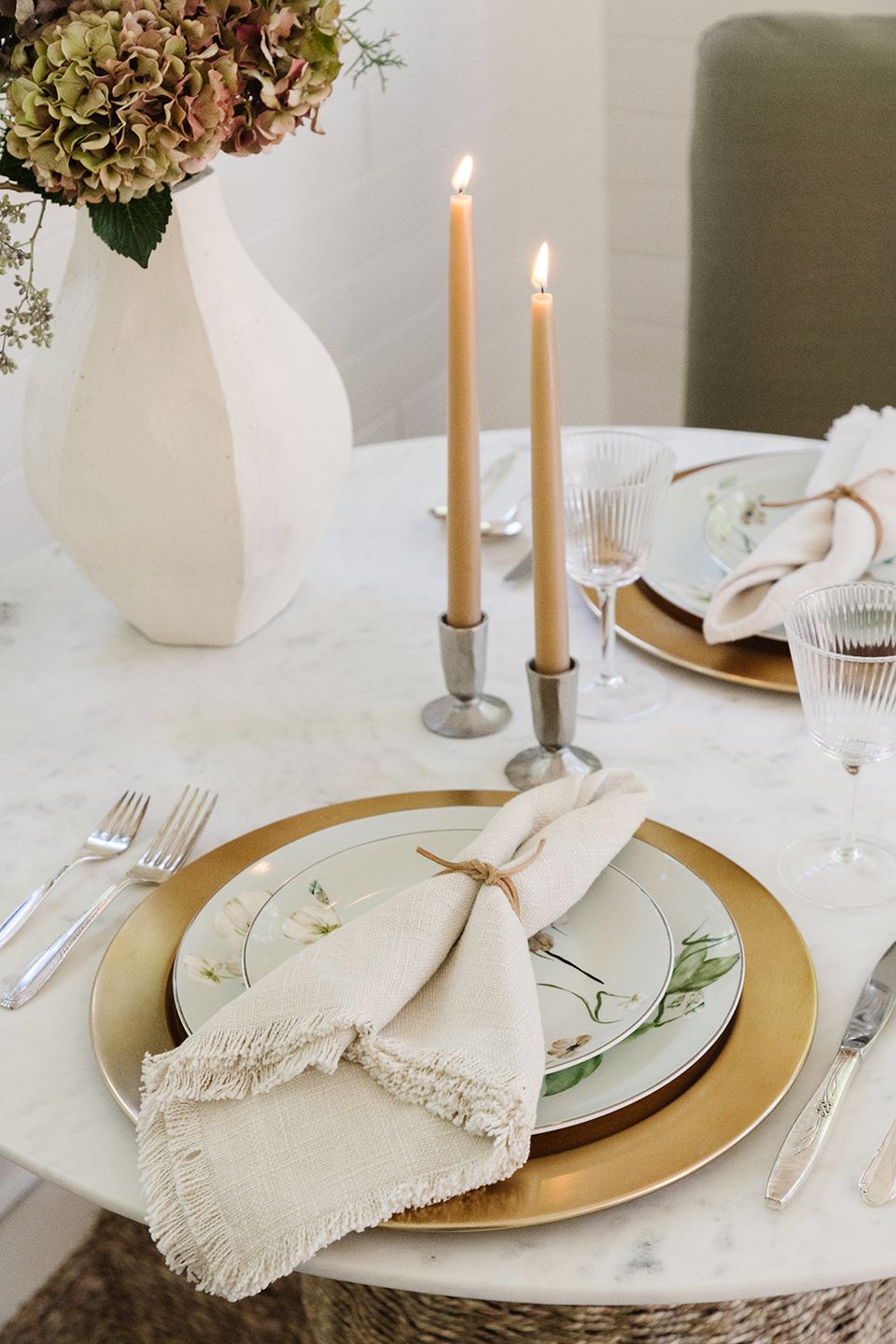 Elegant botanical tablescape with gold chargers, cream napkins, blush candles, and delicate floral plates