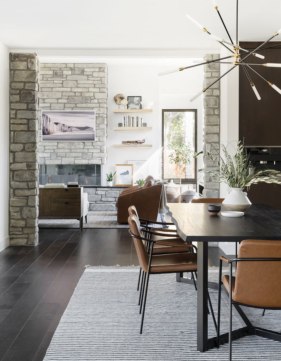Modern industrial space with exposed brick fireplace, dark dining table, leather chairs, and brass geometric pendant light