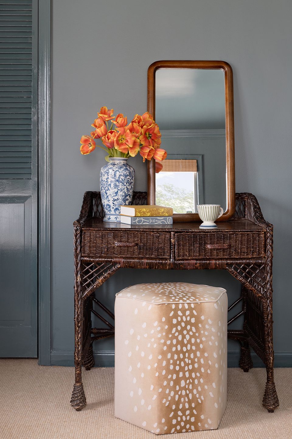 Sophisticated entryway with slate gray walls, woven console, coral flowers, and rounded wooden mirror.