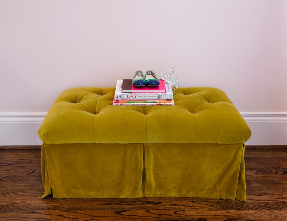 Chartreuse velvet bench with gathered skirt against pale lavender wall, styled with stacked books and accessories.
