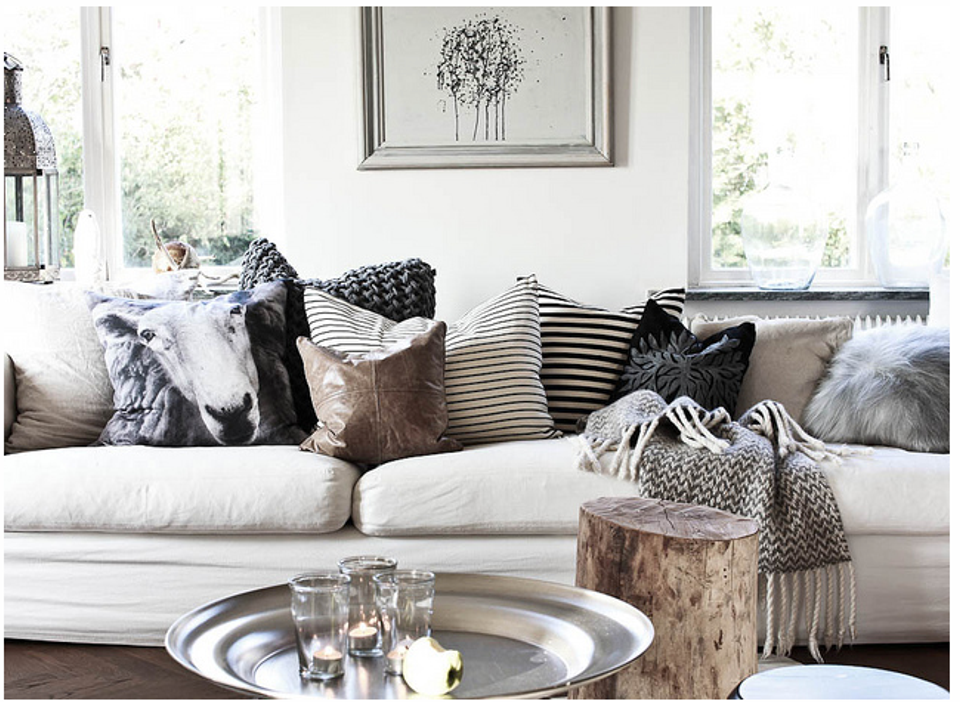 Modern neutral seating nook with layered textured pillows, patterned blankets, and peaceful monochromatic design