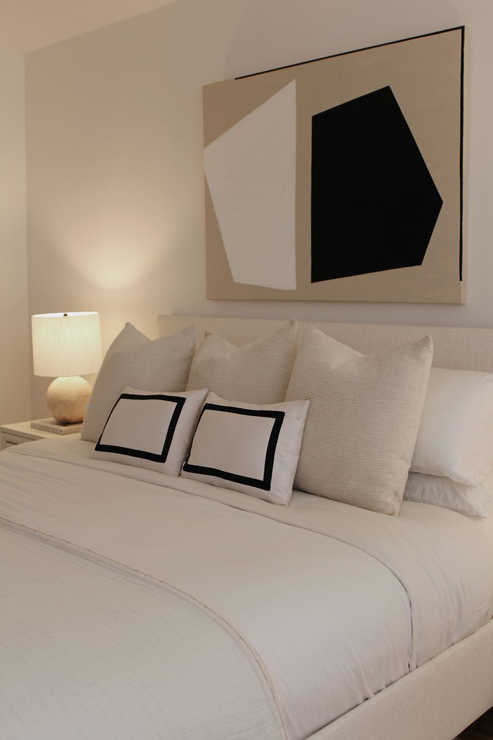 Minimalist bedroom with neutral beige accent wall featuring abstract black and white artwork