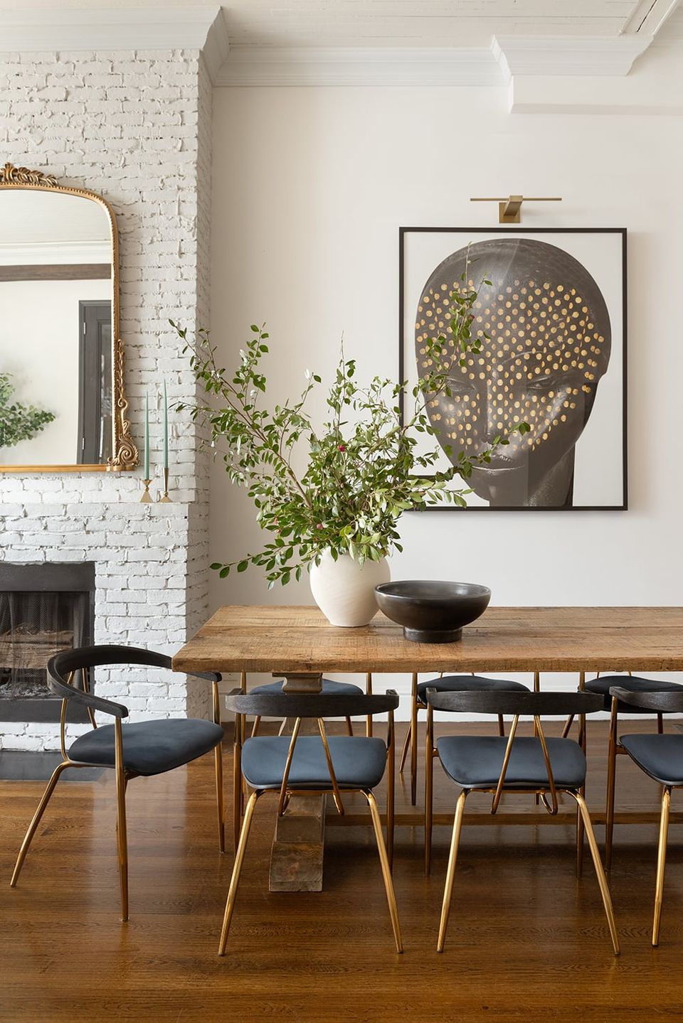 Modern mid-century dining room with warm wood table, black chairs, white brick fireplace, and botanical artwork creating a sophisticated, minimalist gathering space.