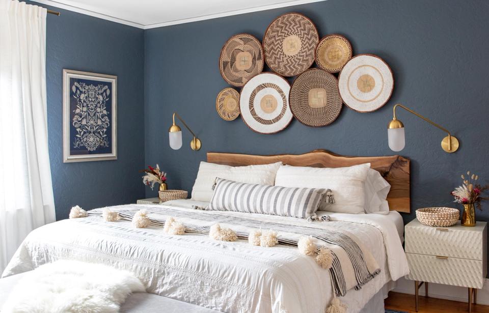 Serene bedroom with deep blue accent wall, woven basket wall display, and neutral bedding creating a calm, nature-inspired coastal aesthetic.