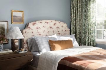 Cozy cottage bedroom with soft blue walls, floral headboard, and sage-green drapes