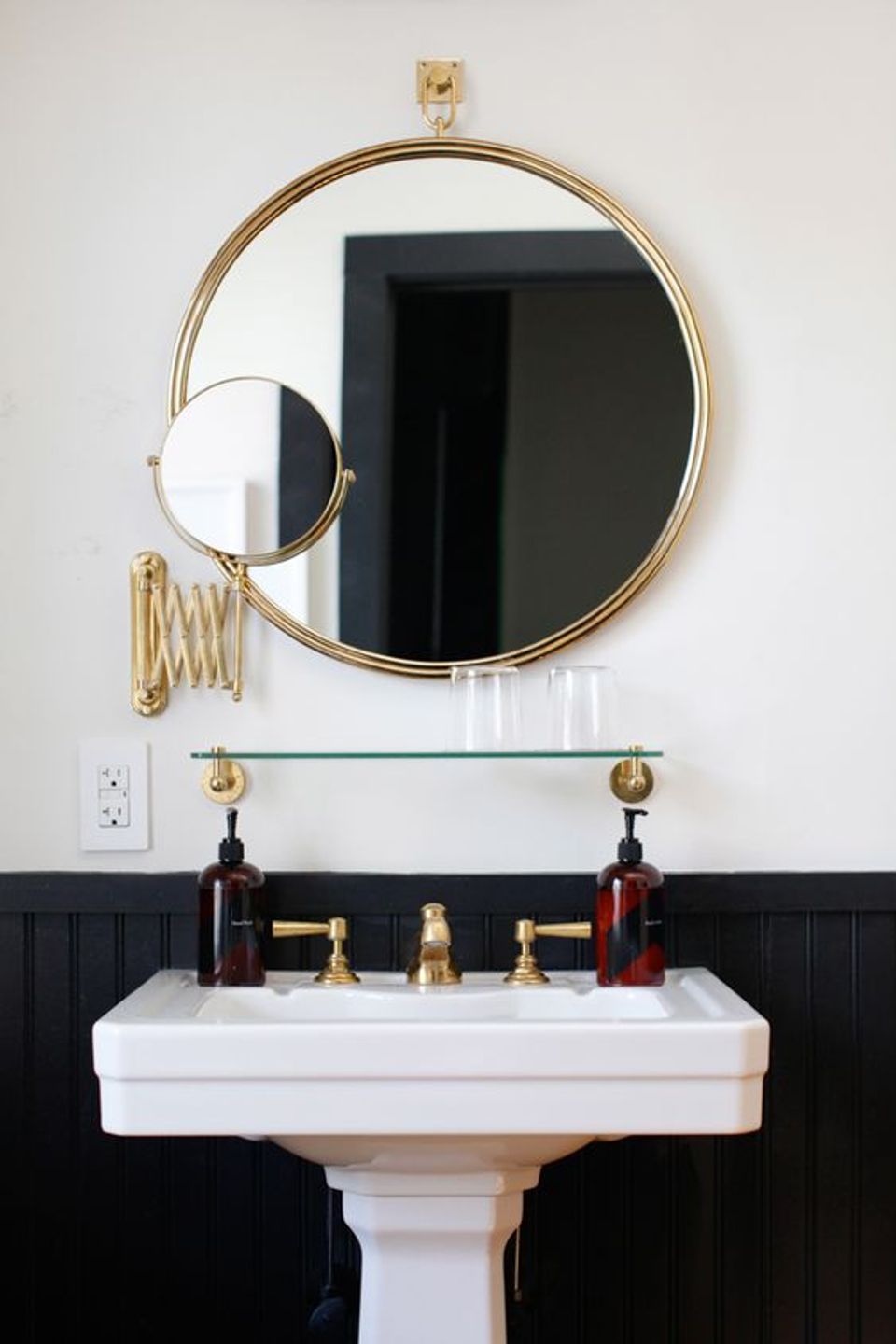 Modern luxury powder room with split black and white paneling, brass-framed mirrors, and pedestal sink
