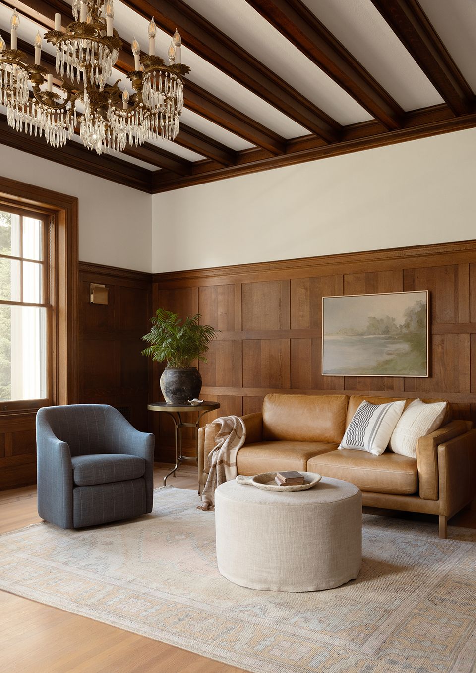 Traditional library-style room with cognac leather sofa, charcoal blue chair, and dark wood paneling.
