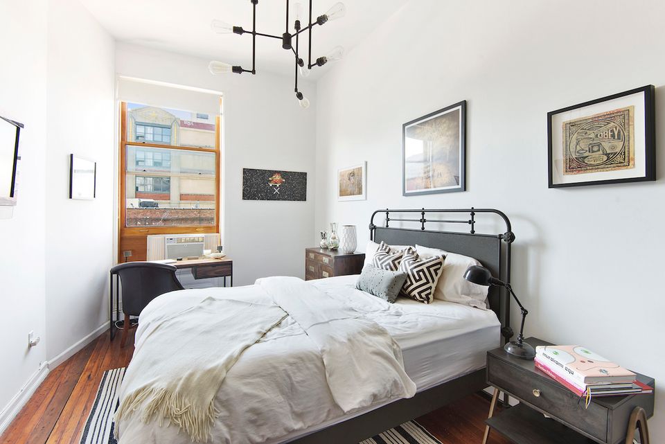 Industrial bedroom with metal bed frame, pendant lighting, and warm wood floors creating a modern minimalist aesthetic.